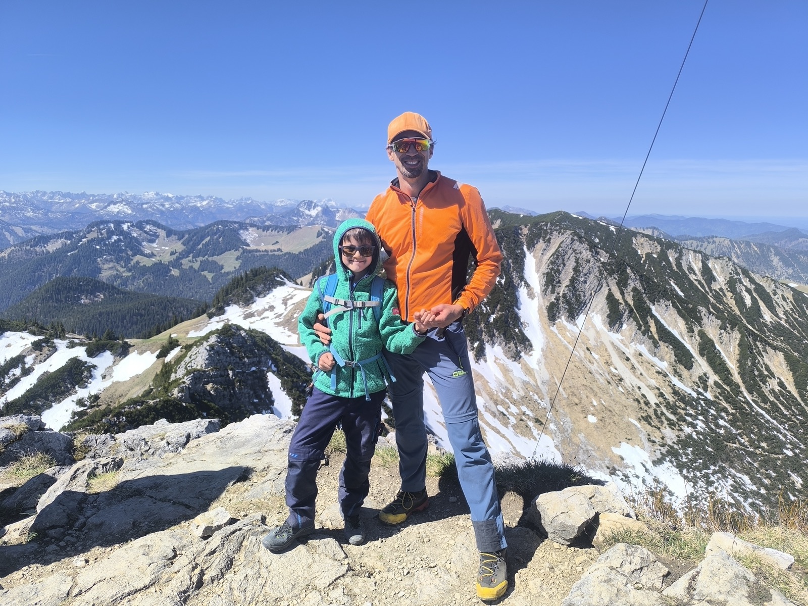 Vater und Sohn auf einem Gipfel, im Hintergrund schneebedeckte Berge
