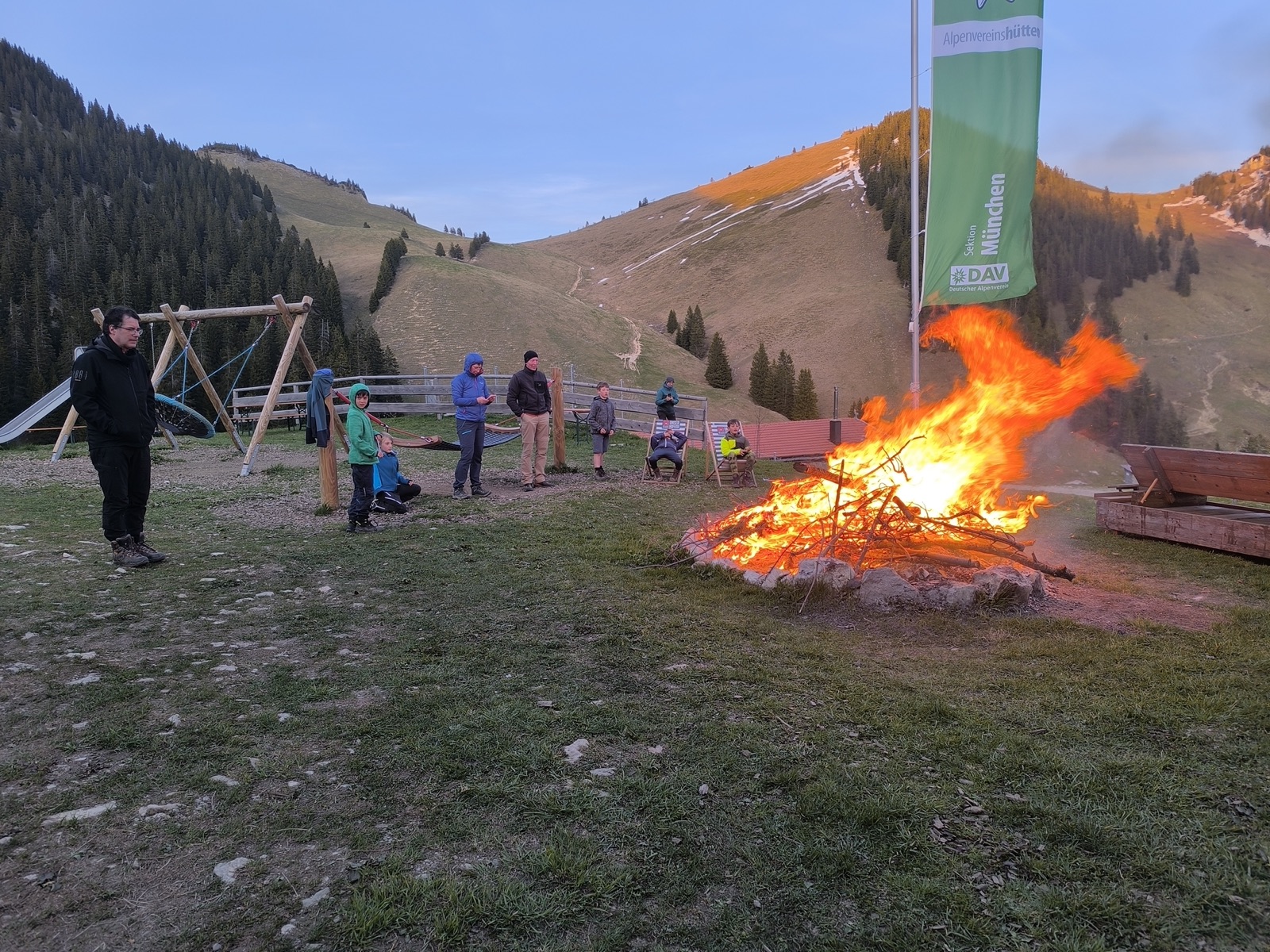 Gruppe am Lagerfeuer vor einer Alpenvereinshütte am Abend